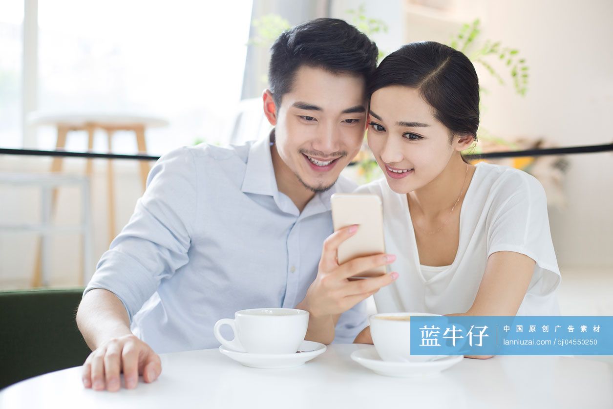 快乐的年轻情侣在咖啡店使用手机