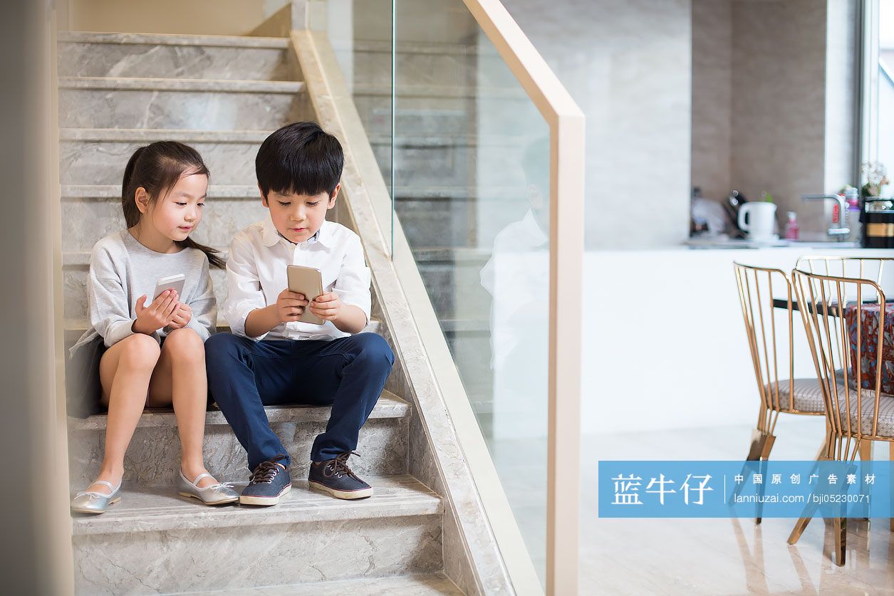 小男孩和小女孩坐在楼梯上玩手机