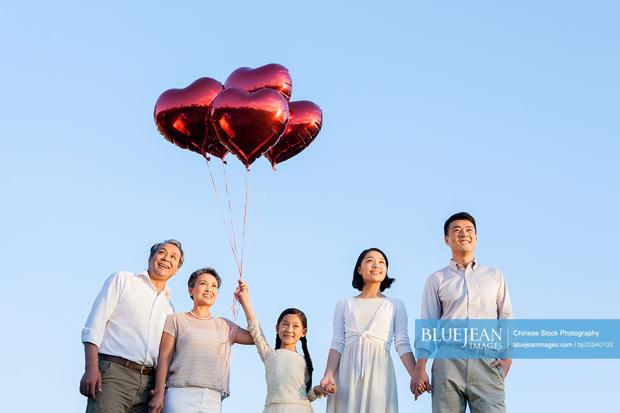 Happy Chinese family with red heart shape balloons in a park