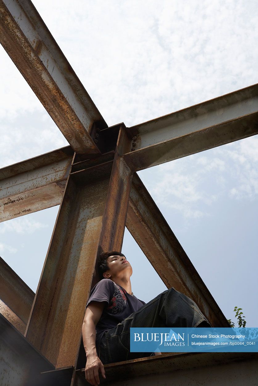 Young Chinese man sitting on a beam in a construction site