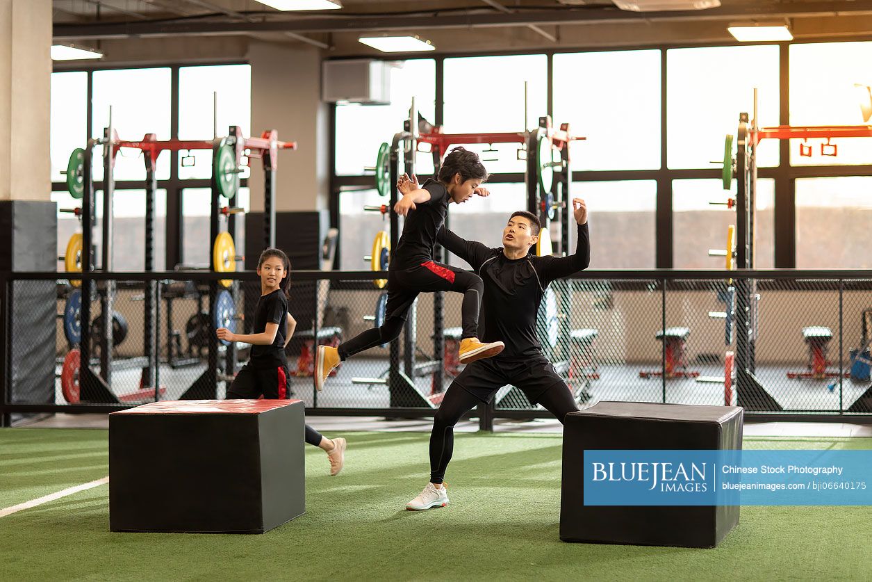 Active Chinese children having exercise class with their coach in gym