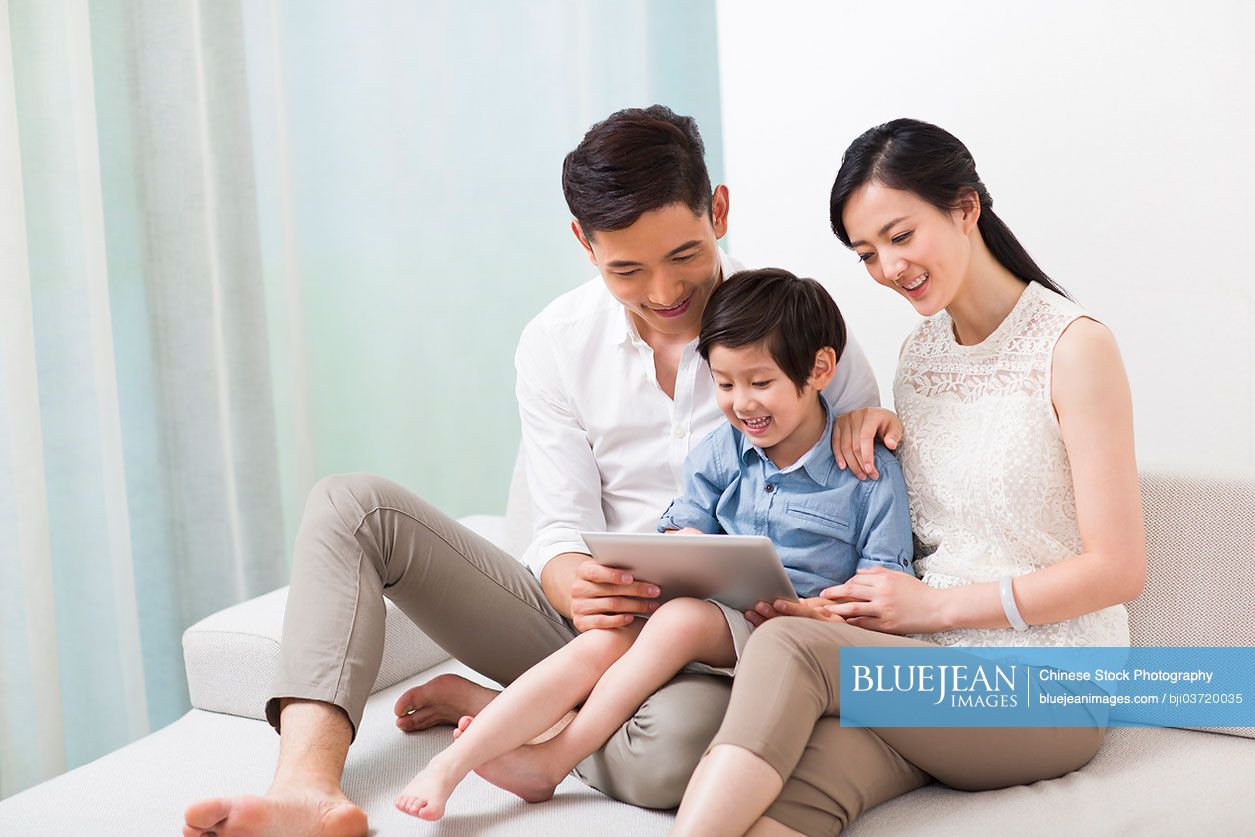 Cheerful young Chinese family using digital tablet on sofa