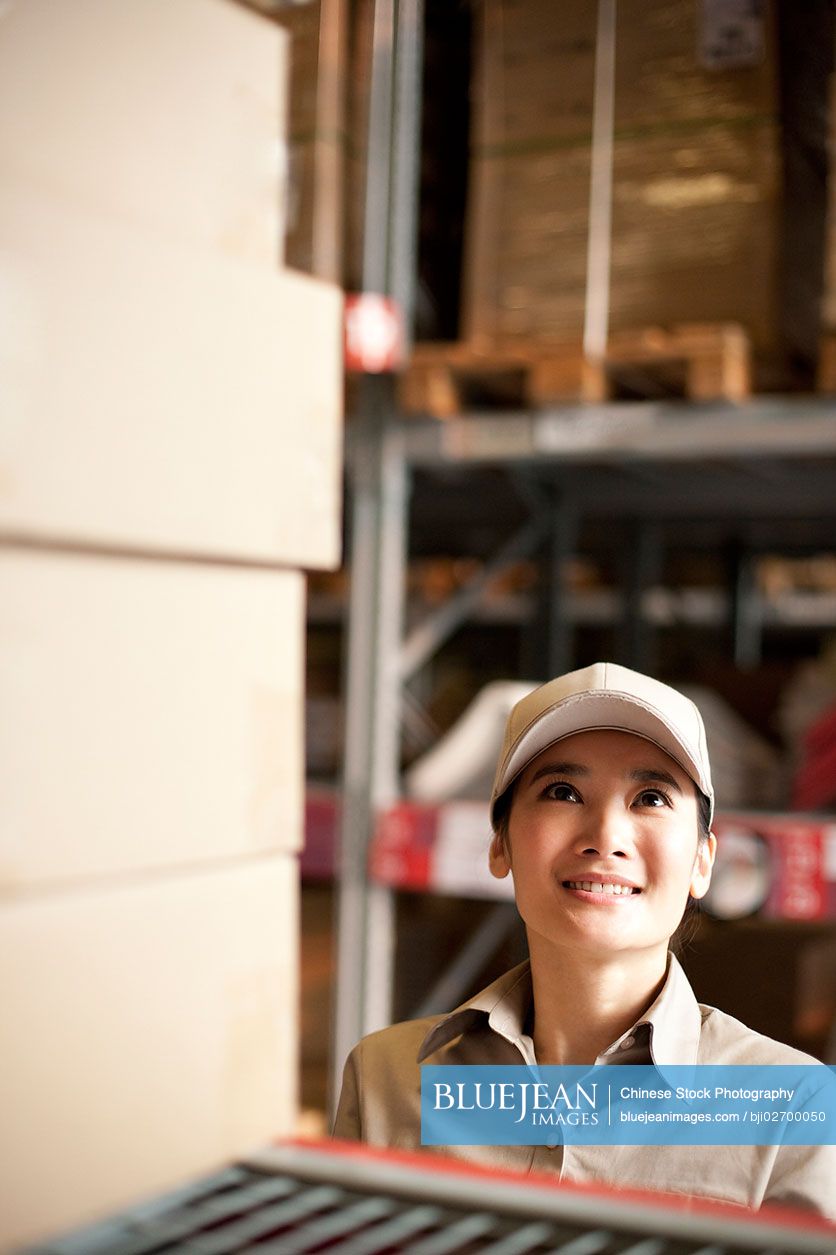 Female Chinese warehouse worker looking at boxes