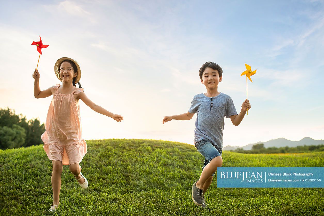 Two Chinese children playing paper windmill on meadow