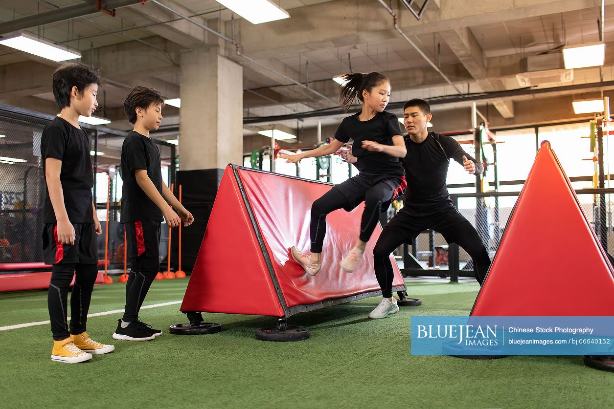 Active Chinese children having exercise class with their coach in gym