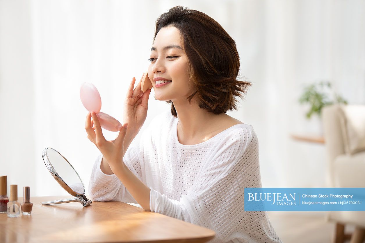 Young Chinese woman applying makeup at home