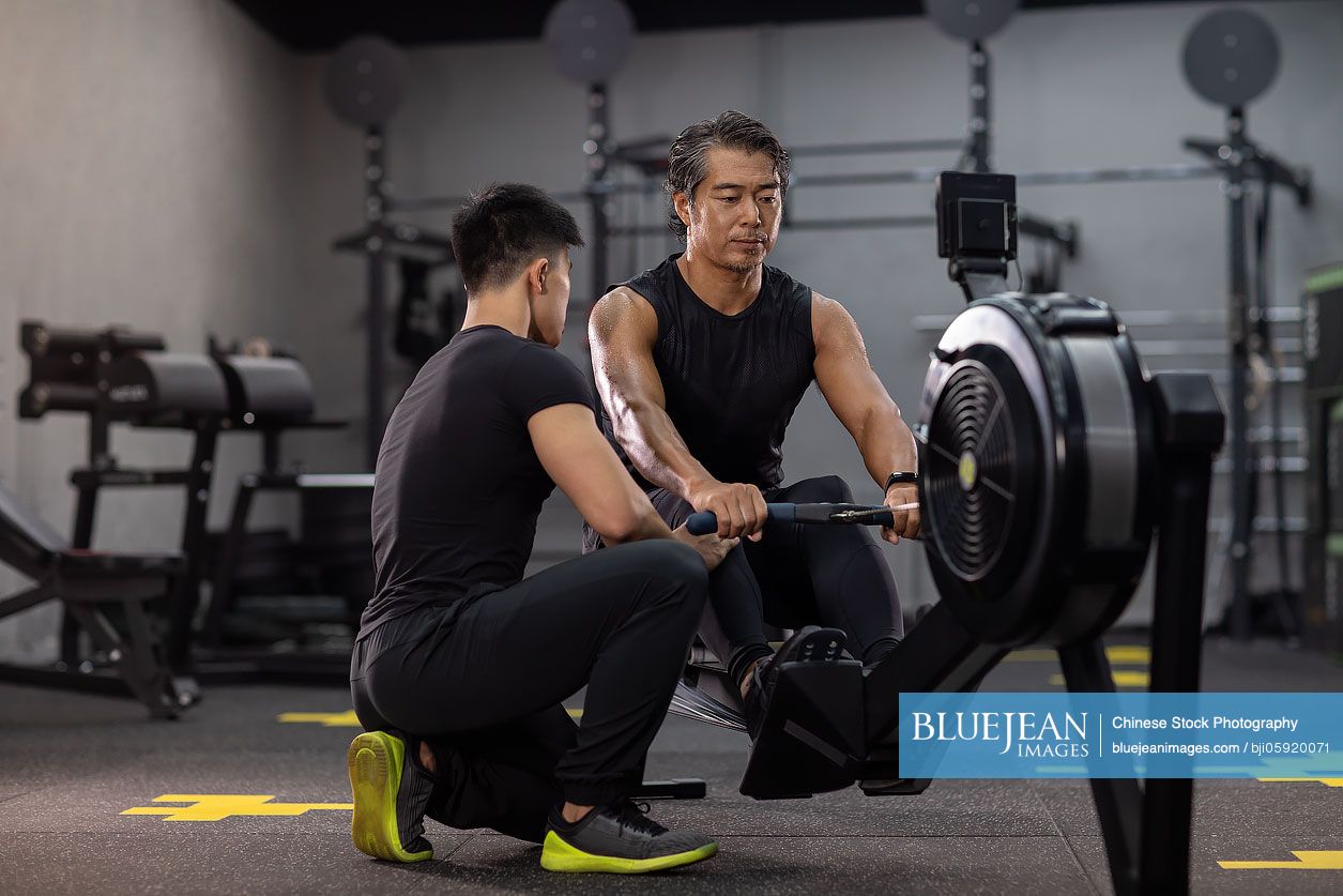 Mature Chinese man working out with personal trainer at gym