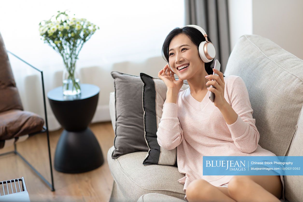 Happy young Chinese woman wearing headphones on sofa