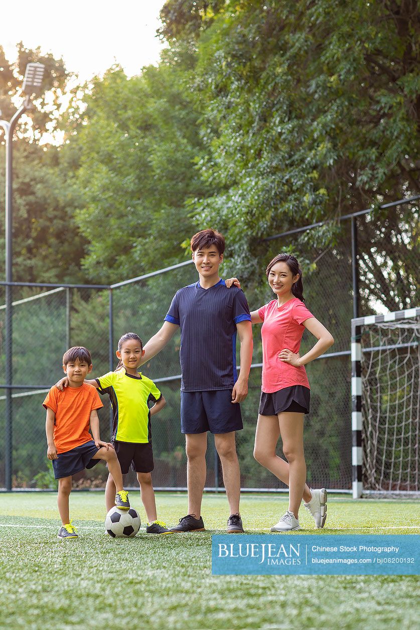 Happy young Chinese family playing football on soccer field