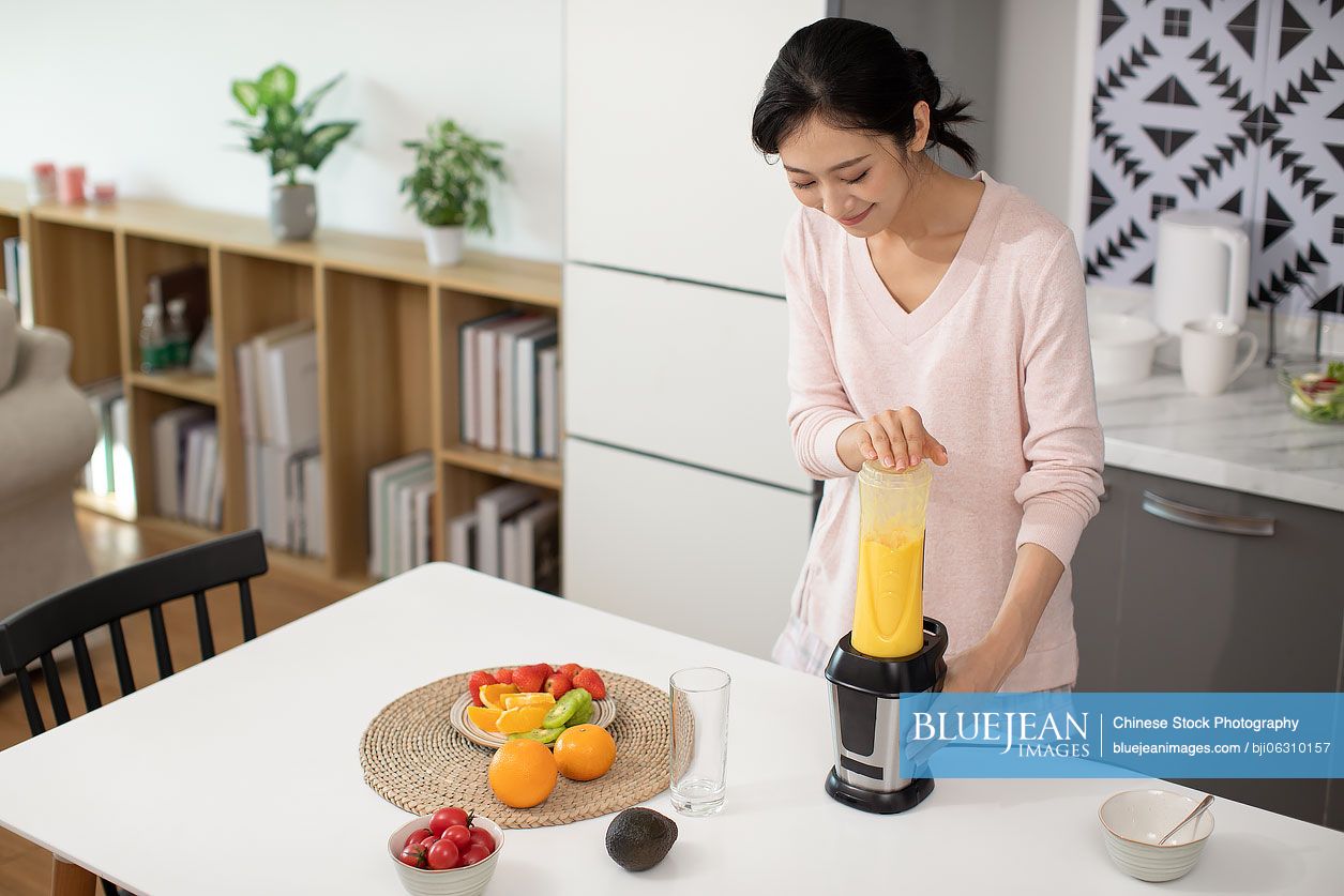 Happy young Chinese woman making juice at home