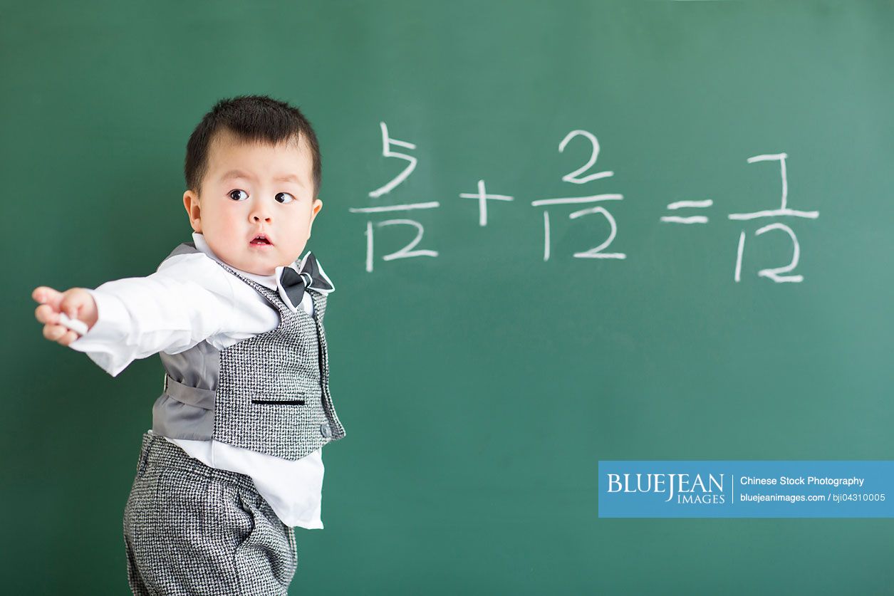 Cute Chinese baby doing mathematics on blackboard