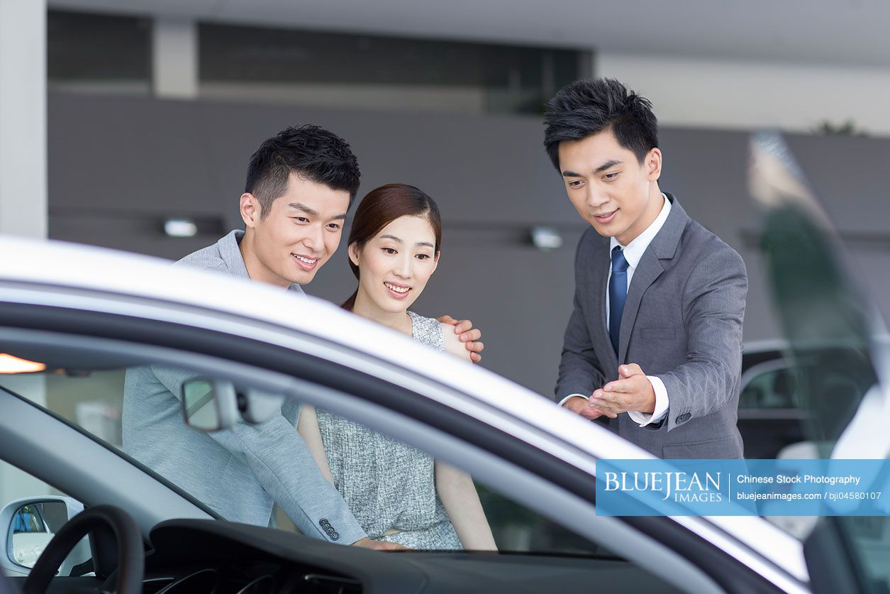 Young Chinese couple choosing car in showroom