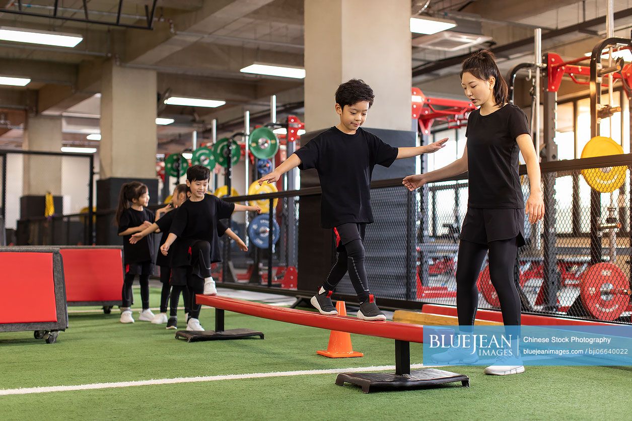 Active Chinese children having exercise class with their coach in gym