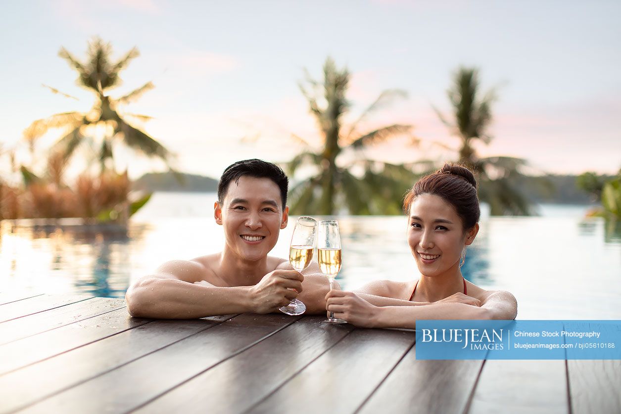 Happy young Chinese couple drinking champagne in swimming pool