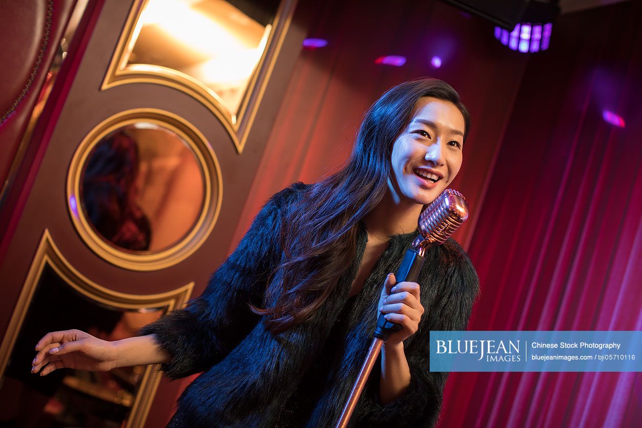 Happy young Chinese woman singing karaoke in nightclub