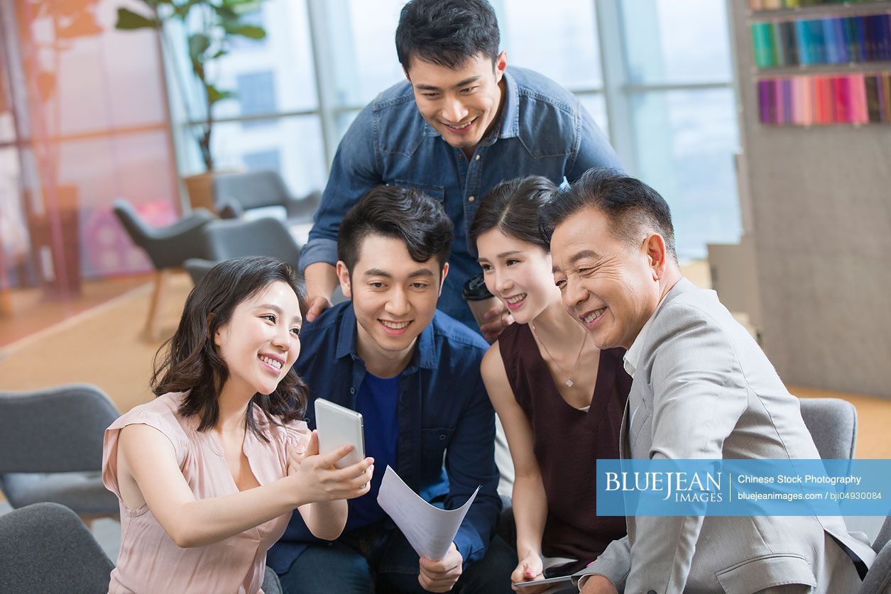 Chinese businesswoman showing smart phone to colleagues