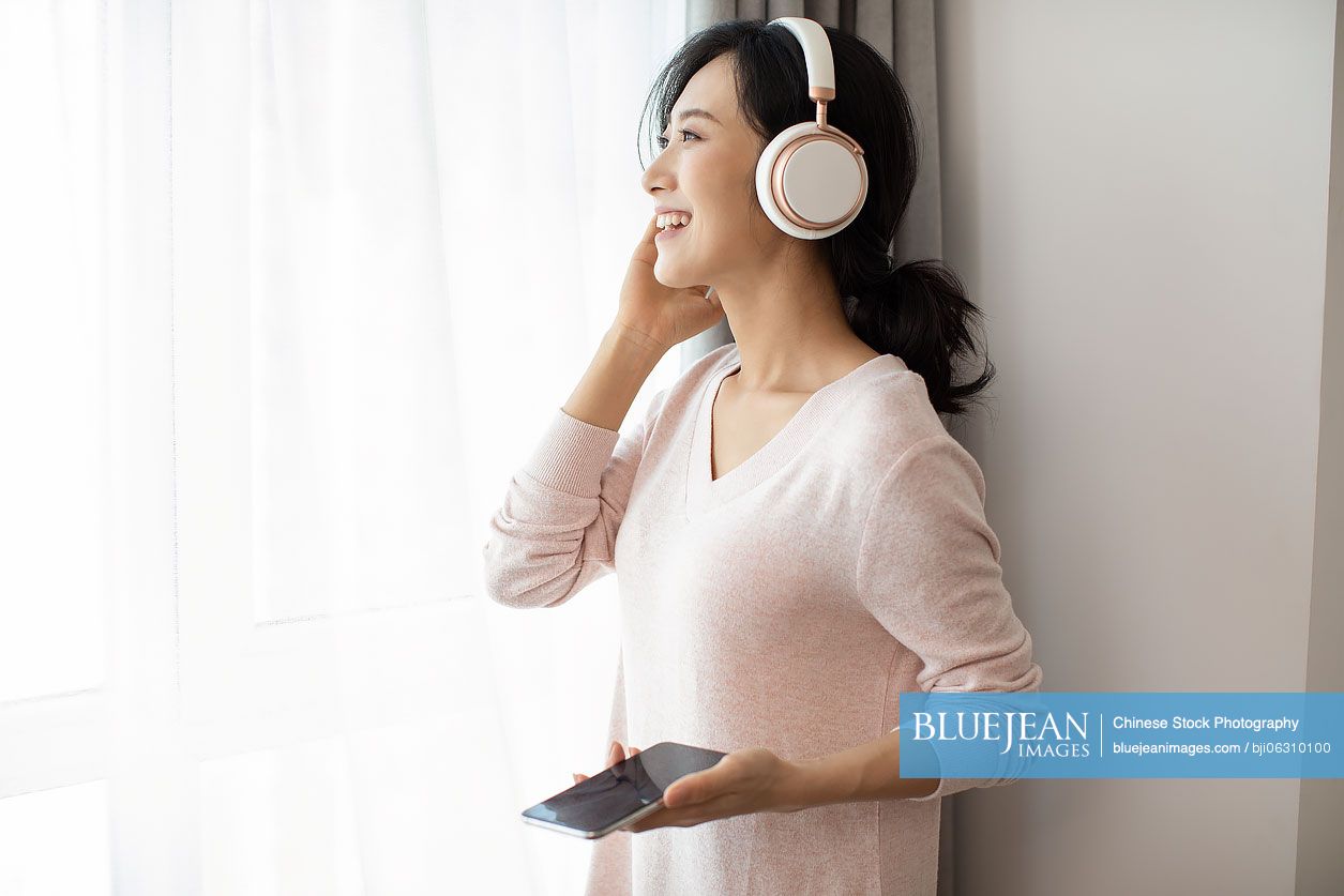 Happy young Chinese woman listening to music in living room