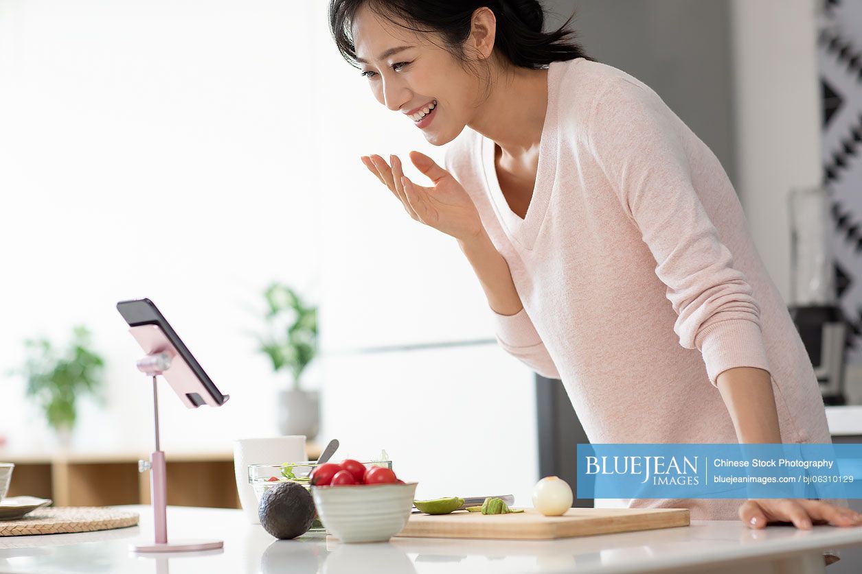 Happy young Chinese woman cooking in kitchen