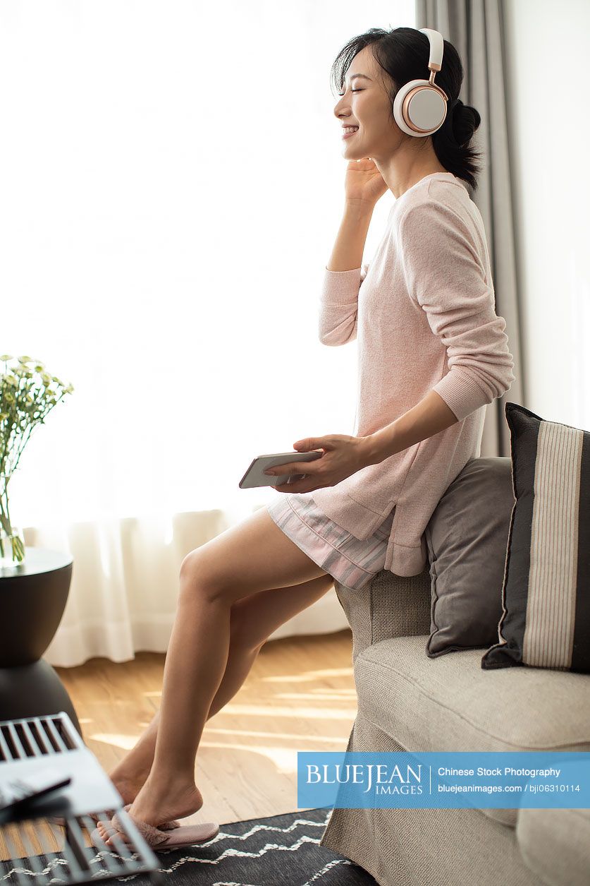 Happy young Chinese woman listening to music in living room