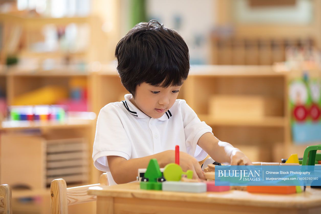 Little Chinese boy playing train set in classroom