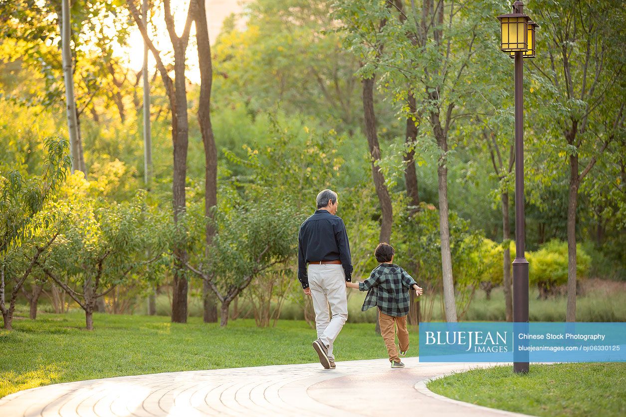 Happy Chinese grandfather and grandson walking in park