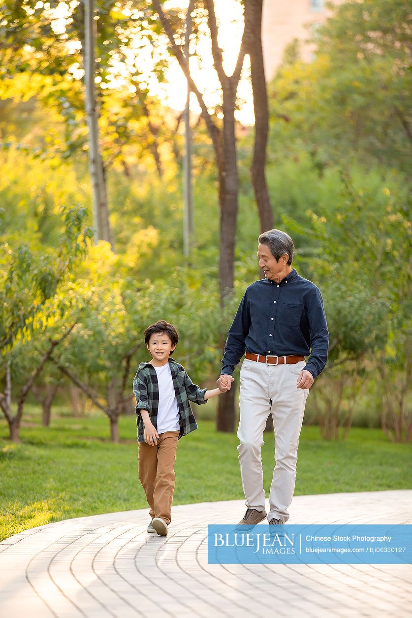 Happy Chinese grandfather and grandson walking in park