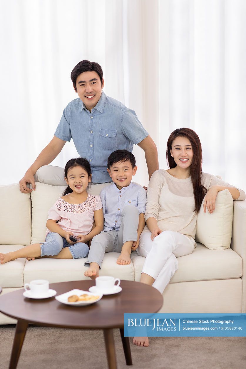 Happy young Chinese family watching TV in living room