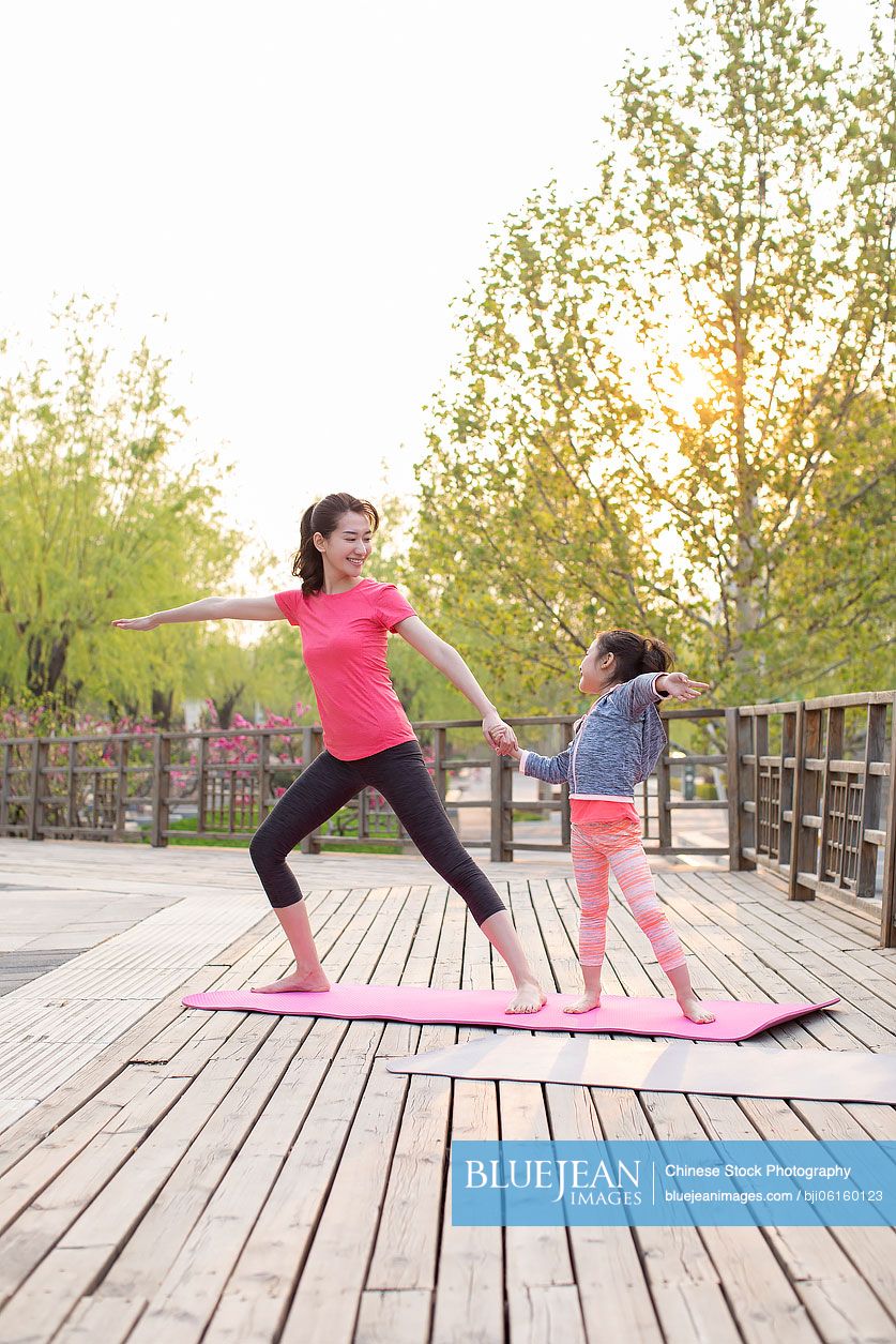 Happy Chinese mother and daughter doing yoga outdoors