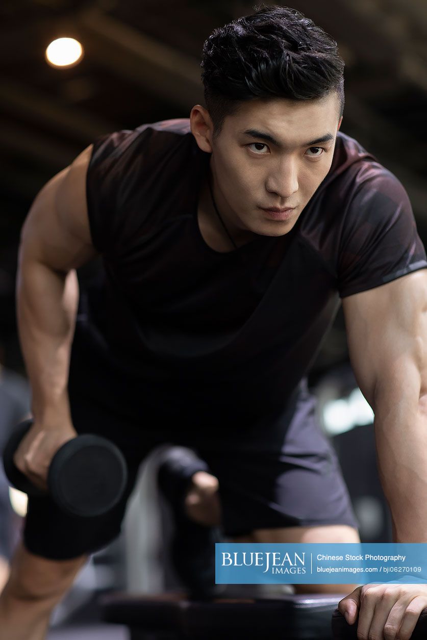 Young Chinese man working out with dumbbell at gym