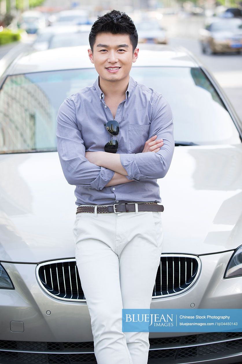 Young Chinese man leaning against his car