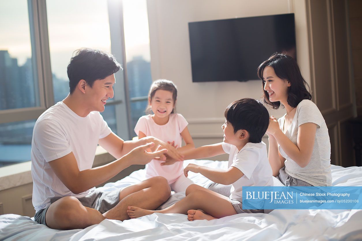 Cheerful young Chinese family having fun on a bed