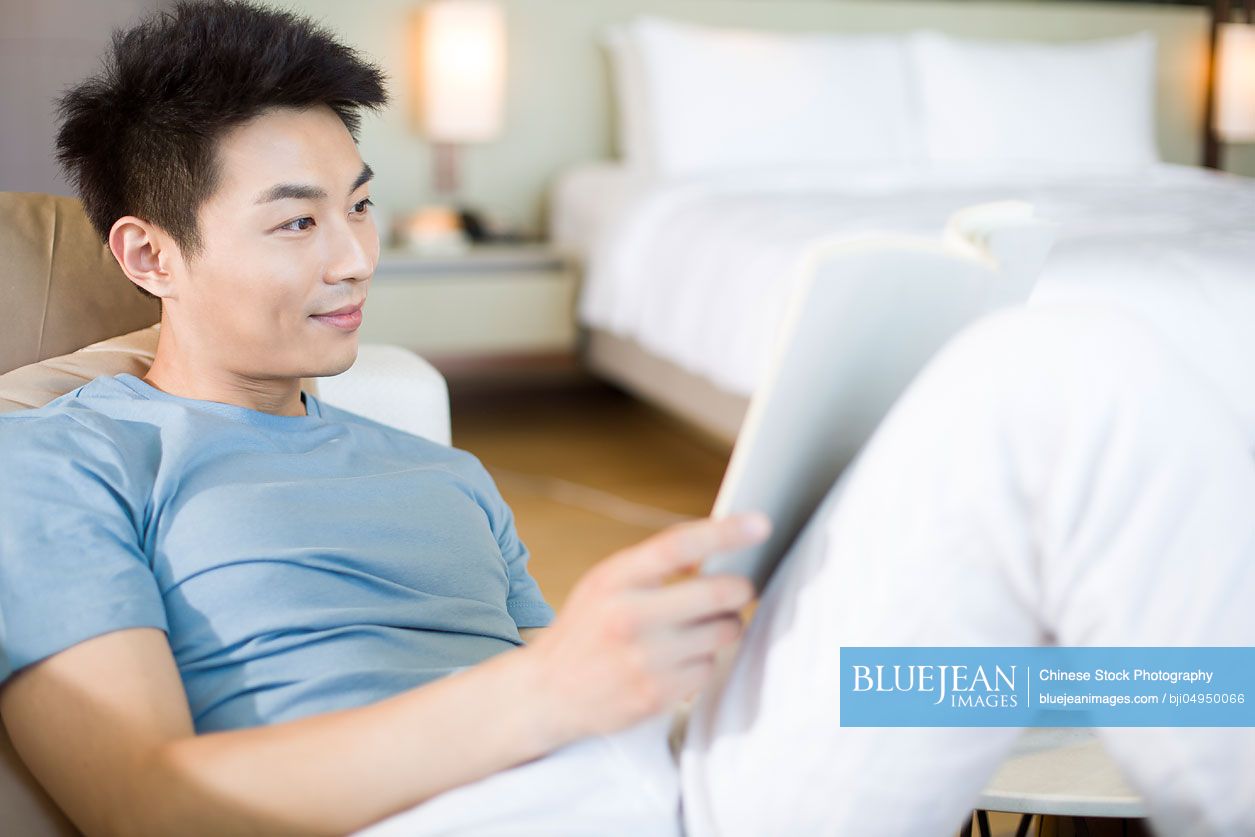 Young Chinese man reading a book on the sofa