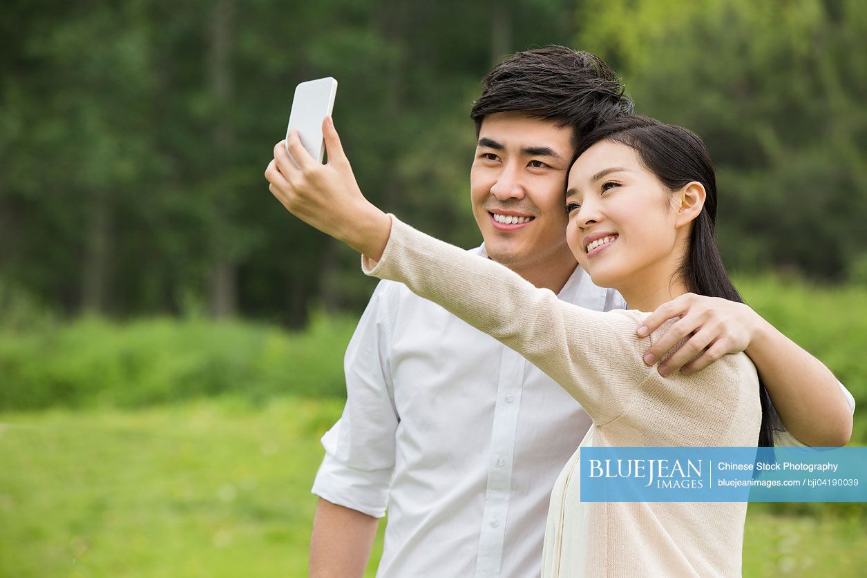 Young Chinese couple taking pictures of themselves with smart phone