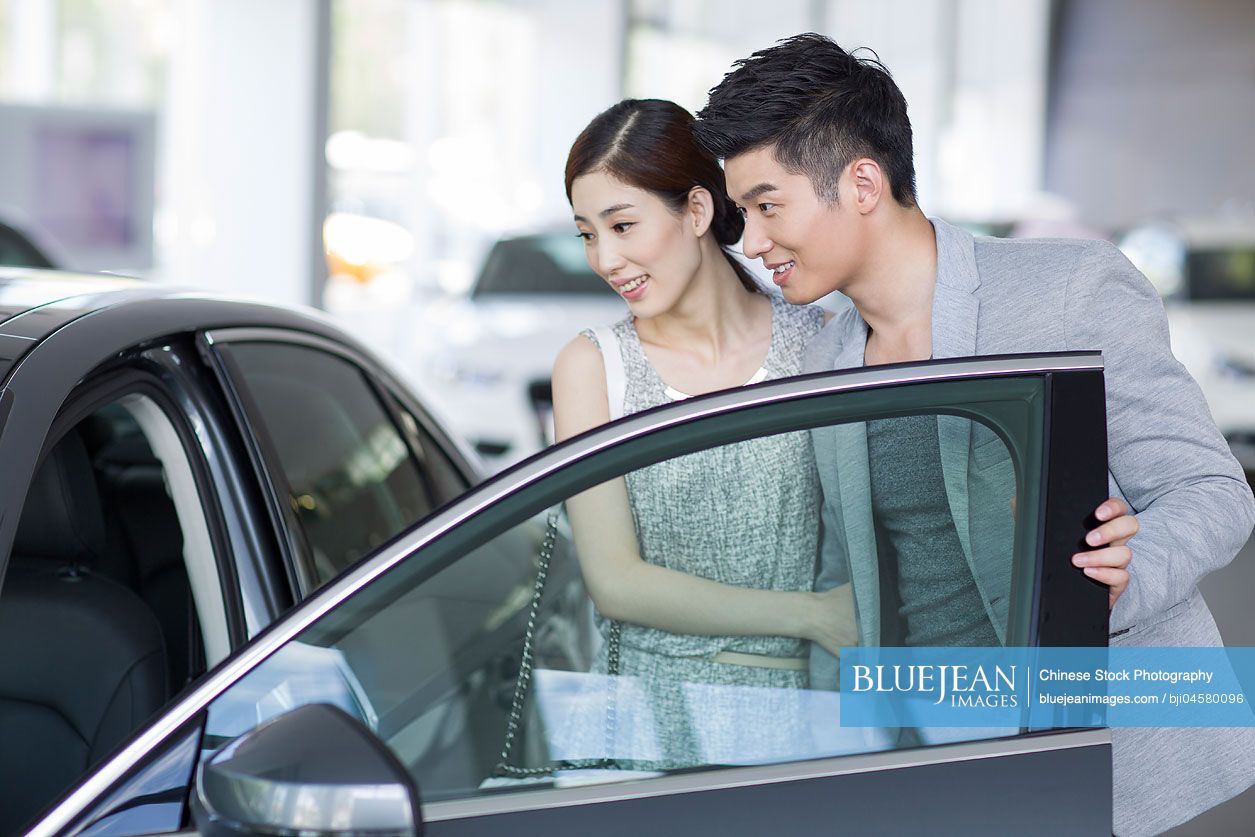 Young Chinese couple looking at new car in showroom