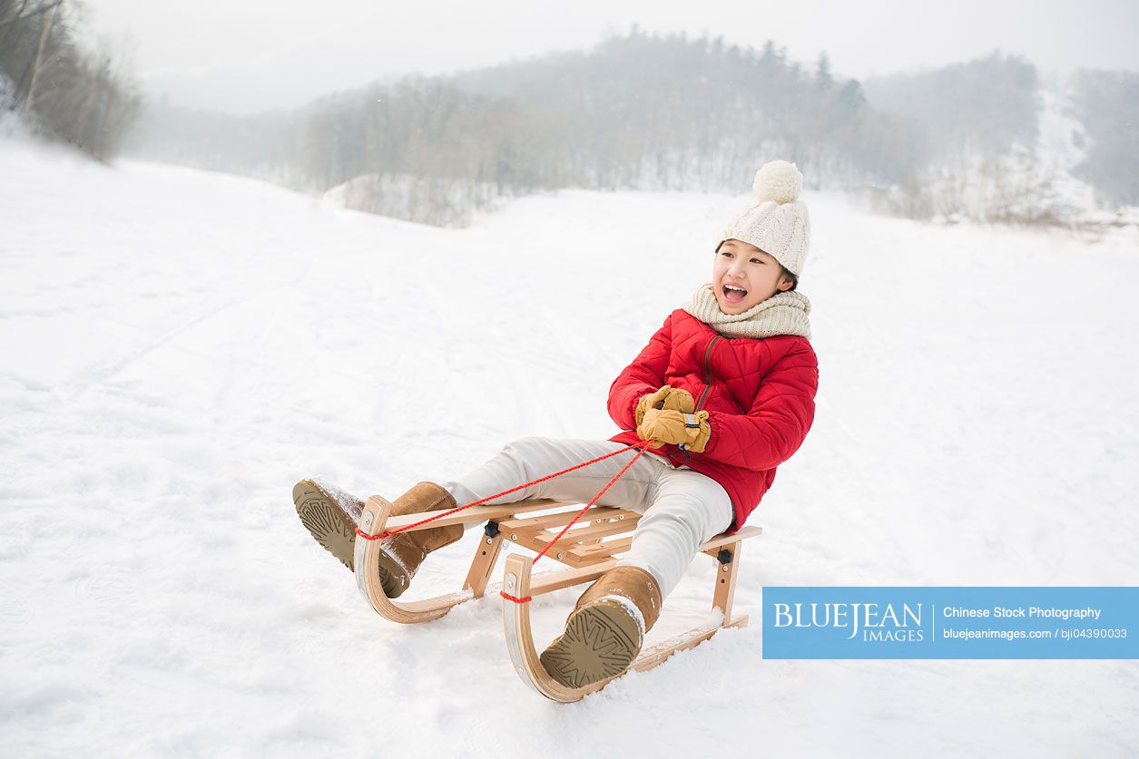 Happy Chinese girl sliding on a sled