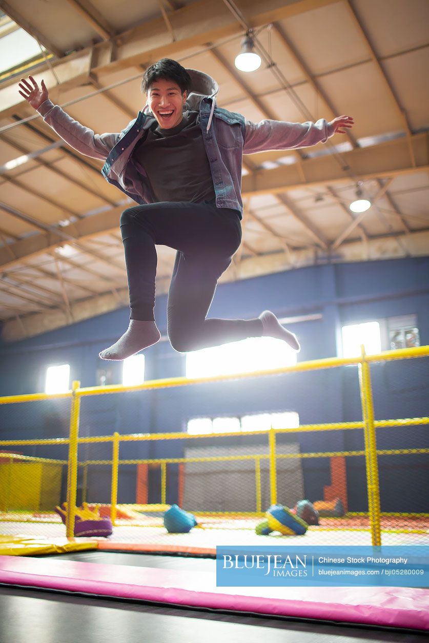 Happy young Chinese man jumping on trampoline
