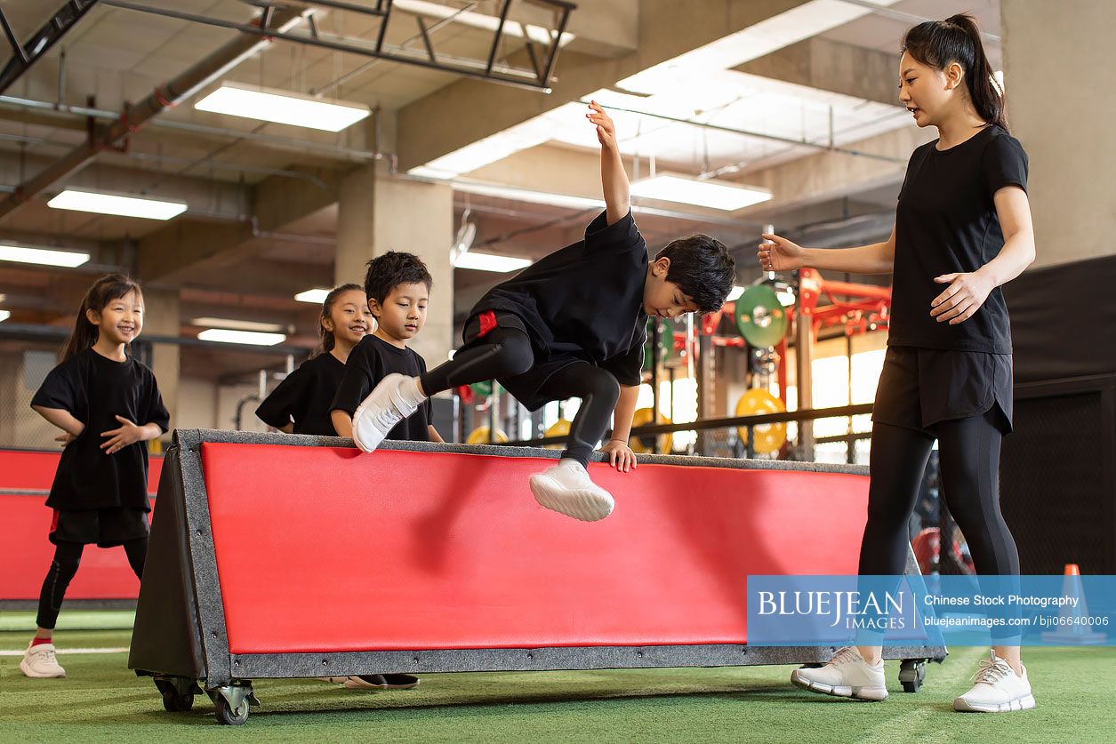 Active Chinese children having exercise class with their coach in gym