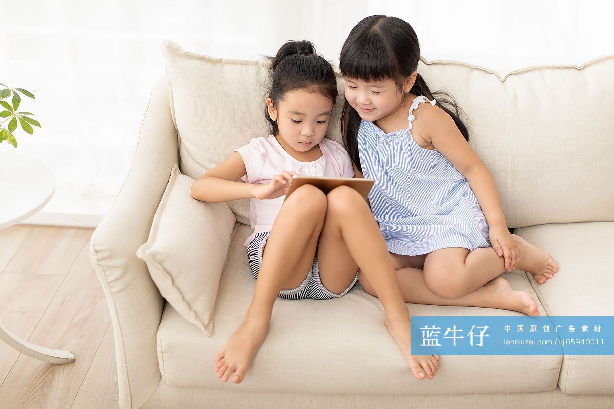 两个小女孩在沙发上玩平板电脑