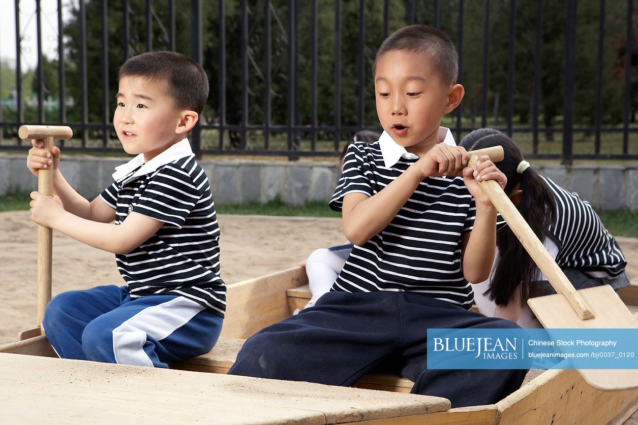 Young Chinese Children Seated In A Boat In A Sandpit