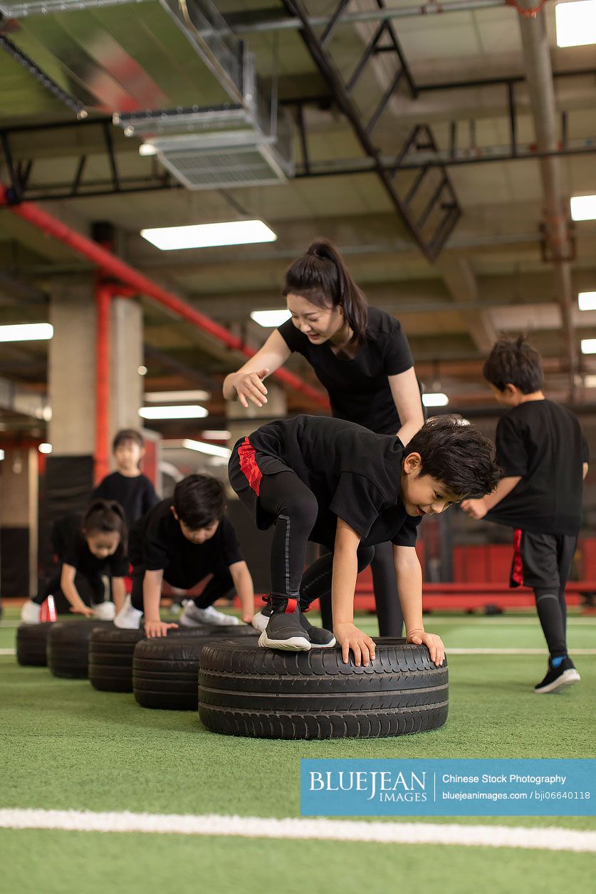 Active Chinese children having exercise class with their coach in gym