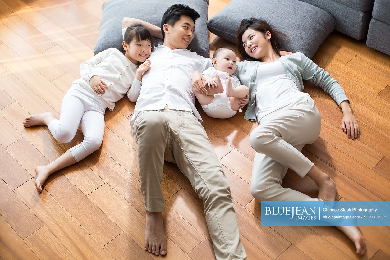 Happy young Chinese family resting on wooden floor