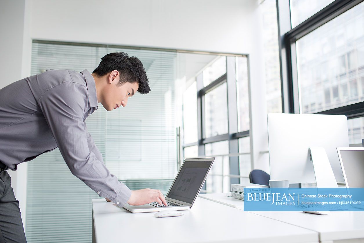 Young Chinese businessman using laptop in office