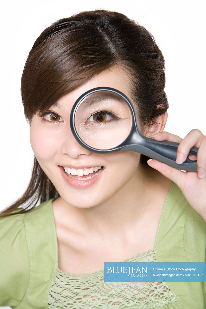 Portrait of young Chinese woman looking through magnifying glass