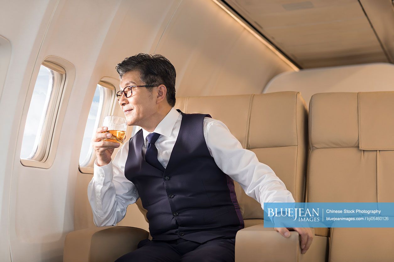 Senior Chinese businessman drinking whiskey on airplane