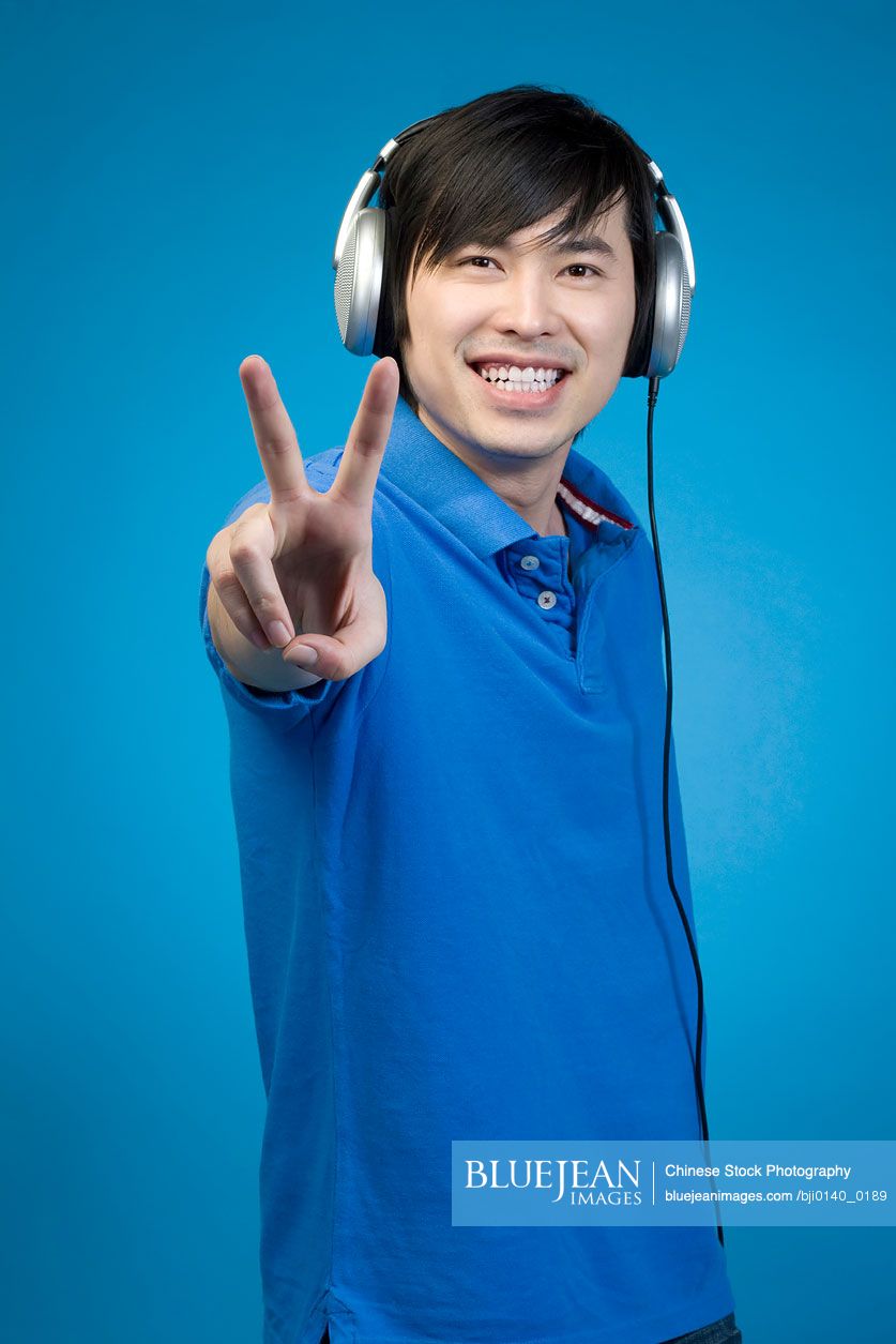 Chinese man listening to headphones and giving peace sign