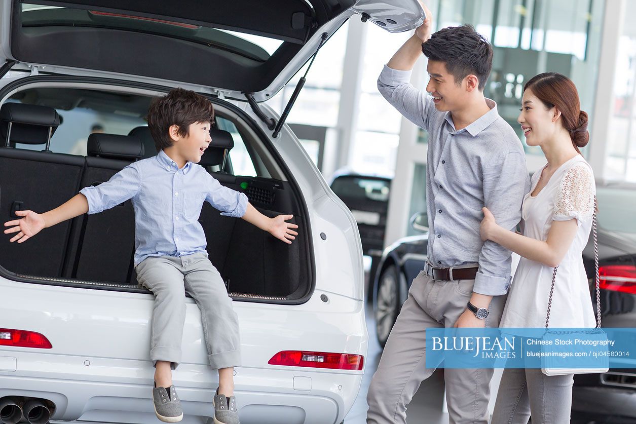 Young Chinese family choosing car in showroom
