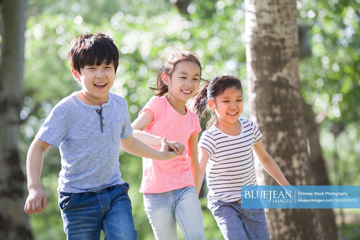 Happy Chinese children holding hands running in woods