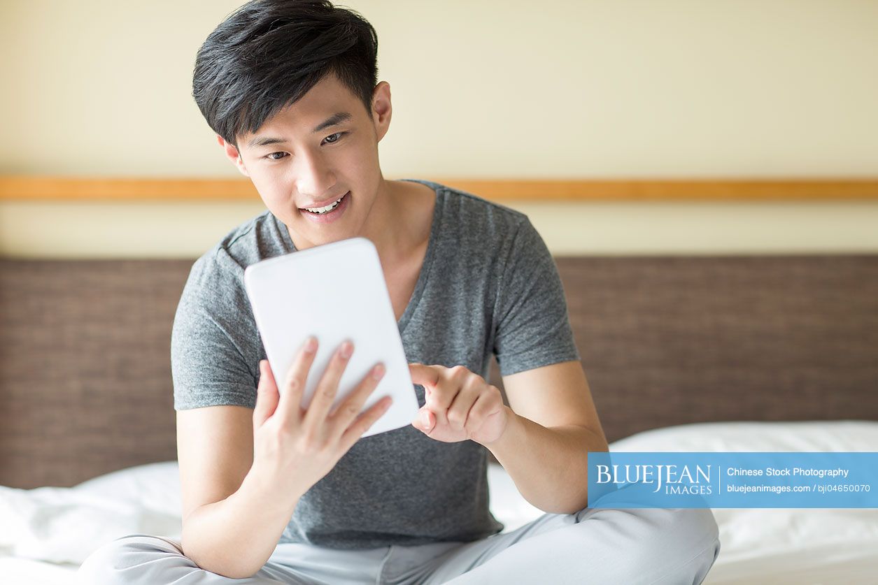 Young Chinese man using digital tablet on bed