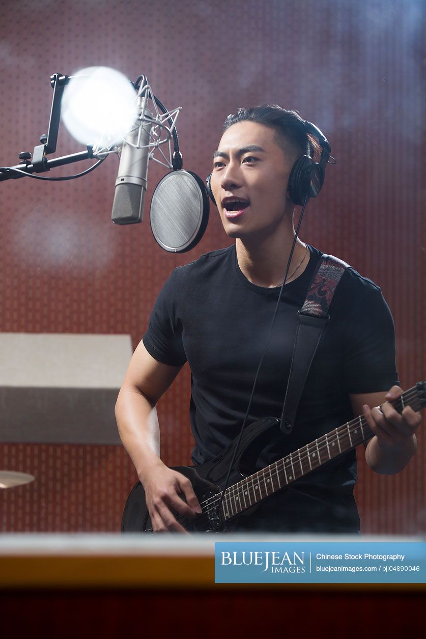 Young Chinese man singing with guitar in recording studio