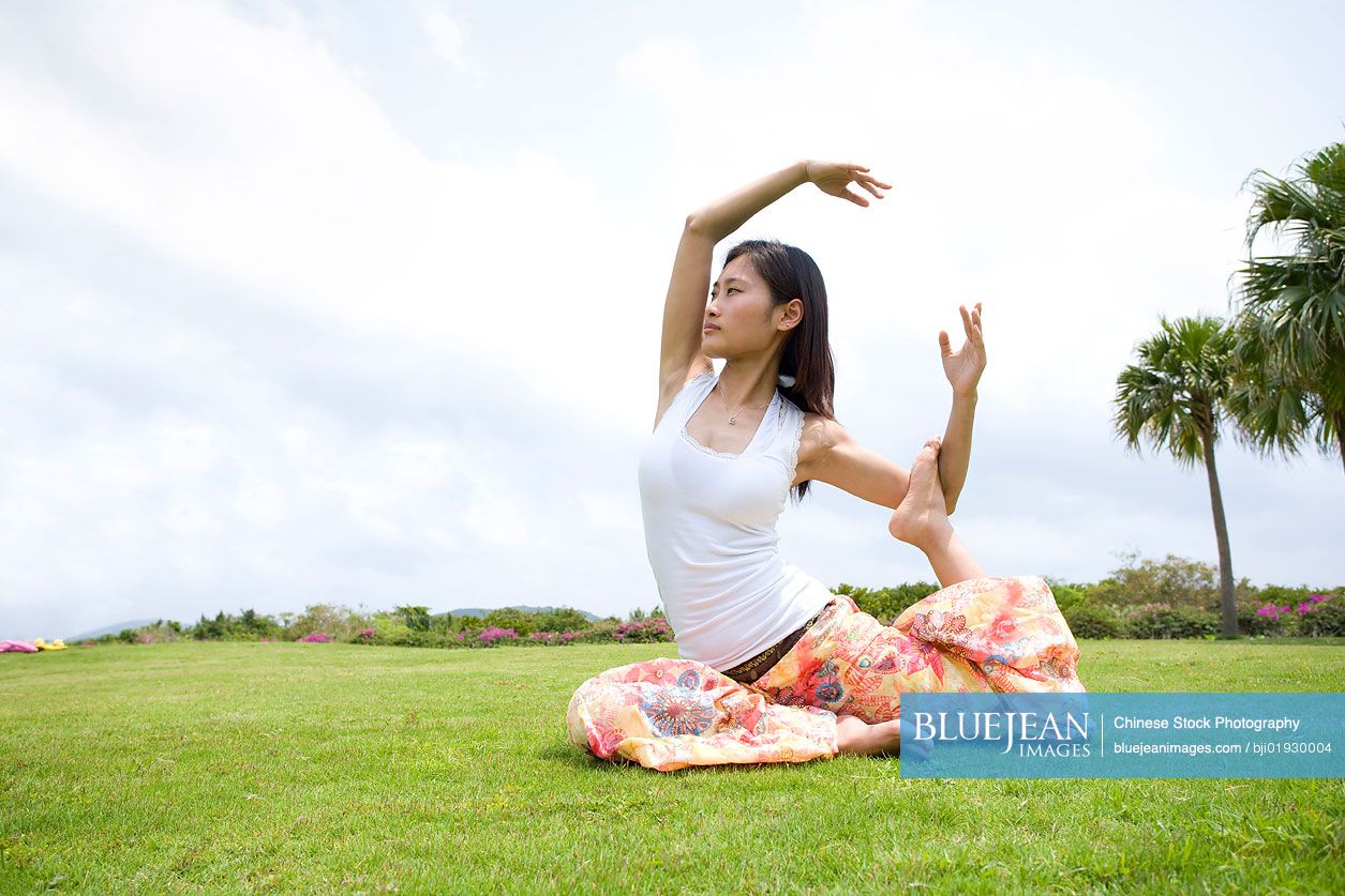 Young Chinese woman doing yoga in grass
